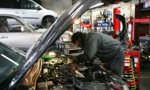Mekaniker arbetar med en bilmotor i ett garage. En annan bil står i bakgrunden. Här erbjuds stor service.