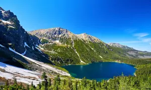 Górskie Morskie Oko lśni w słońcu, otoczone zielonymi lasami i skalistymi szczytami Tatr.