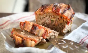Un délicieux pain de viande, garni de tomates et de lardons, est servi sur une assiette blanche.