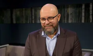Szymon Bobrowski w garniturze i okularach, z brodą, wygląda jakby opowiadał o swoich filmach, serialach i programach.