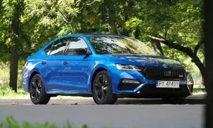 Błękitna Skoda Octavia RS 2025 z czarnymi felgami, zaparkowana wśród zieleni.