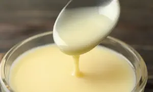 Gęste, kremowe mleko skondensowane spływa z łyżki do szklanej miseczki. Idealne do deserów i ciast, jak w tym przepisie.