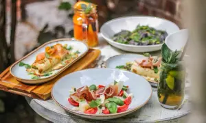 Stół z daniami: naleśniki z łososiem, sałatka z szynką parmeńską i pomidorkami, czarne spaghetti, napoje.
