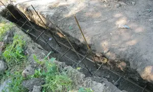 Zbrojenie do fundamentu ogrodzeniowego w wykopie. Metalowe pręty tworzą siatkę, gotową na zalanie betonem.