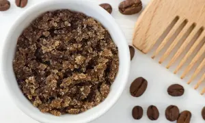 Domowy peeling do skóry głowy z kawy w białej miseczce, obok drewniany grzebień i ziarna kawy.