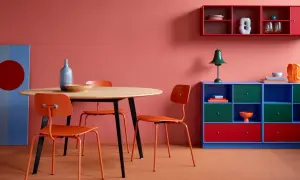 Ein Essbereich mit roten Stühlen und einem runden Holztisch. Die Wand ist korallenrot, und ein blaues Regal mit roten Akzenten steht daneben. Welche Farbe passt zu Rot? Blau und Grün sind tolle Kontraste!