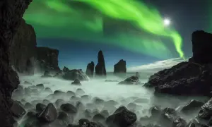 Grüne Nordlichter tanzen über einer felsigen Küste. Ein magischer Septemberabend auf einer Insel, wo das Meer in Nebel gehüllt ist.