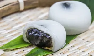 Co to jest mochi? Dwa białe, okrągłe ciastka ryżowe z ciemnym nadzieniem, podane na bambusowej tacce z zielonymi liśćmi.
