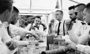 Panowie w eleganckich koszulach i szelkach świętują kawalerski przy cygarach i drinkach. Wesołe zabawy na kawalerski w męskim gronie.