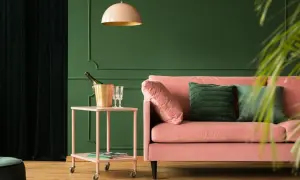 Różowa kanapa i złoty kubełek na szampana na stoliku. Wnętrze w odcieniach zieleni, gdzie kolory metali dodają elegancji.