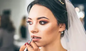 Panna młoda z welonem i biżuterią otrzymuje makijaż ślubny glamour. Usta podkreślone błyszczykiem, oczy smoky eye.