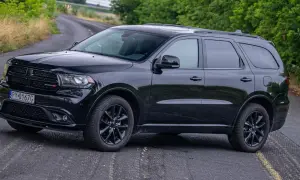 Czarny Dodge Durango 3.6 na krętej drodze, otoczony zielenią.