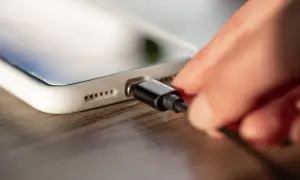 Dłoń podłącza kabel do ładowania białego iPhone'a.