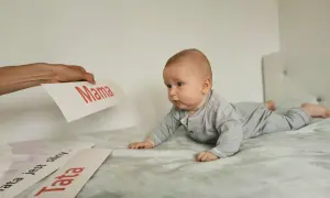 Zaciekawione niemowlę na brzuchu patrzy na kartkę z napisem "Mama". Obok leżą kartki "Tata" i "Tata jest silny".