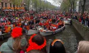 Tłumy ludzi w pomarańczowych strojach świętują dzień króla w Amsterdamie, płynąc łodziami po kanałach.