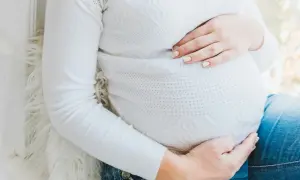 Gravid mage med händer som vilar på den. Kanske känner hon av ont i blygdbenet gravid.