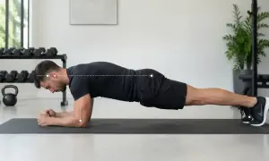 Un homme effectue un gainage planche sur un tapis de gym, le corps droit, soutenu par ses avant-bras et ses pieds.