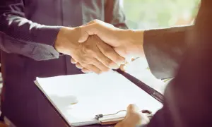 Poignée de main entre deux hommes d'affaires, l'un tenant un dossier, symbolisant un contrat cadre dirigeant conclu.