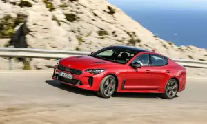 Czerwony Kia Stinger pędzi po krętej drodze nad morzem.
