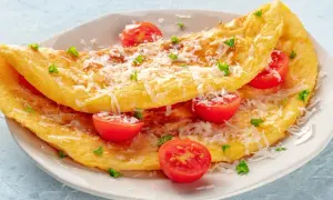 Puszysty omlet z serka wiejskiego, posypany parmezanem i udekorowany pomidorkami koktajlowymi i natką pietruszki.
