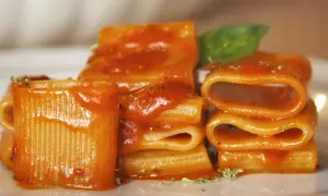Piatto di pasta allo scarpariello, con rigatoni conditi da un sugo rosso e guarniti con basilico fresco.