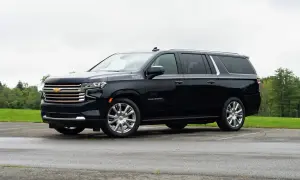 Czarny Chevrolet Suburban High Country z chromowanymi felgami stoi na mokrym parkingu, otoczony zielenią.