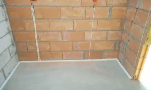 Widoczne przewody w posadzce bez peszla, biegnące od puszek instalacyjnych w ceglanej ścianie do podłogi.