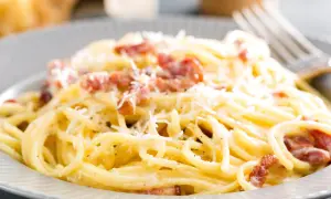 Spaghetti alla carbonara z boczkiem i parmezanem na szarym talerzu.