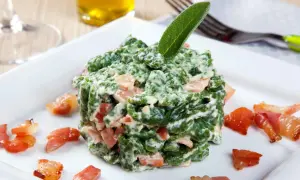 Spätzle verdi cremosi con pezzetti di speck croccante, guarniti con una foglia di salvia. Un piatto invitante.