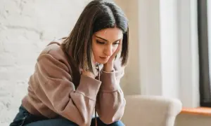 Una joven con las manos en la cara, con expresión de tristeza, parece reflexionar sobre qué es ser pesimista.
