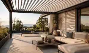 Terrazza con divano e lettino, sotto una pergola con lamelle orientabili, ideali come sistemi oscuranti esterni per finestre, con vista sul mare.