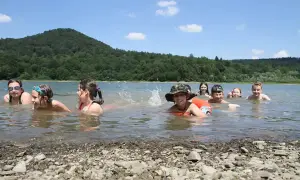 Dzieci kąpią się w górskim jeziorze, ciesząc się letnim dniem. Woda jest czysta, a wokół rozciąga się piękny, zielony las.