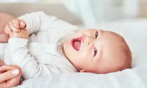 Uśmiechnięte niemowlę w białym body leżące na białym tle.