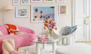 Ein Wohnzimmer im **danish pastel** Stil mit einem pinken Sofa, bunten Bildern und einer Vase voller Blumen.