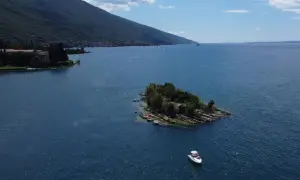 Un'isola verdeggiante nel Lago di Garda, con piccole imbarcazioni ormeggiate e una barca a motore che naviga nelle acque azzurre.
