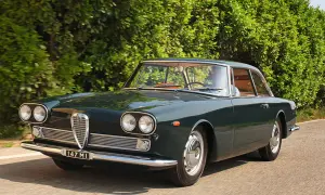 En mörkgrön Alfa Romeo Giulia Sprint GT kör längs en landsväg, en klassisk skönhet bland Alfa Romeo modeller.