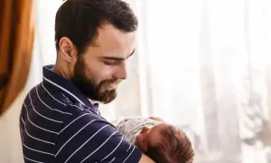 Szczęśliwy ojciec z zarostem tuli noworodka. To piękny czas urlopu ojcowskiego.