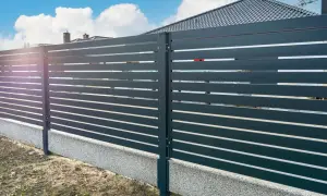 Nowoczesne ogrodzenie z ciemnoszarych paneli. Betonowa podmurówka stanowi solidną podstawę, co zamiast podmurówki pod ogrodzenie można zastosować.