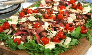 En läcker italiensk grillad biff sallad med körsbärstomater, pinjenötter och parmesan på en bädd av ruccola.
