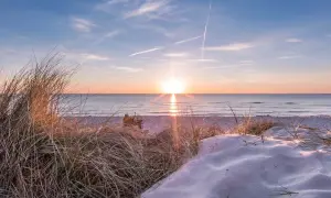 Sonnenuntergang am Strand, ein perfekter Urlaub in Deutschland. Dünen mit Gräsern und Sand, das Meer glitzert.