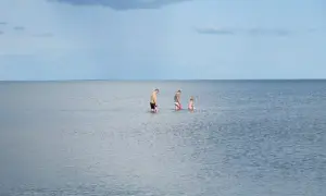 Rodzina brodząca w spokojnym morzu, na tle błękitnego nieba z chmurami.