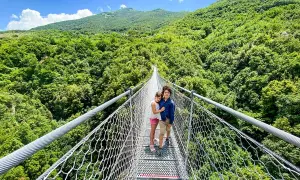 Bambini su un percorso ponte tibetano, circondati da una lussureggiante foresta verde sotto un cielo azzurro.