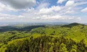 Widok z Kłodzkiej Góry na zielone wzgórza i pola. Niebo z chmurami.
