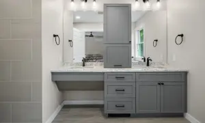 A modern, gray, freestanding vanity with dual sinks and a tall cabinet stands against a light gray wall.