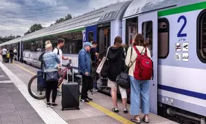 Ludzie wsiadają do pociągu PKP. Wśród nich starszy pan, młodzi ludzie z rowerem i bagażami. Może właśnie korzystają z **pkp zniżki dla niepełnosprawnych stopień lekki**?