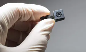 Main d'une personne portant un gant blanc tenant une minuscule caméra. Comment savoir si on a une caméra chez soi ?