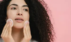 Donna con capelli ricci scuri pulisce il viso con dischetti di cotone, affrontando brufoli e punti neri per una pelle radiosa.