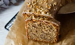 Ein saftiger Nusskuchen mit Zuckerguss und gehackten Nüssen, angeschnitten auf Backpapier.