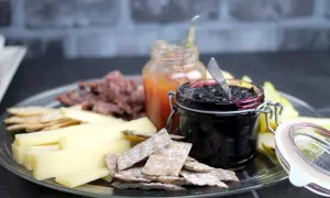 Ostbricka med kex, kött, päron och två sorters marmelad till ost. En burk med mörk bärsylt och en med ljus fruktmarmelad.