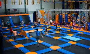 Dzieci skaczą na trampolinach w największym parku trampolin w Polsce. W tle widać ściankę wspinaczkową i tor przeszkód.